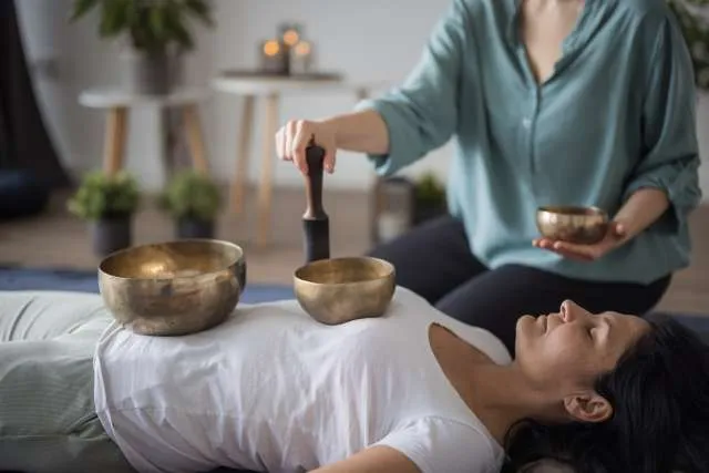 Facilitadora tocando cuencos tibetanos sobre persona tumbada en sesión individual de sonoterapia