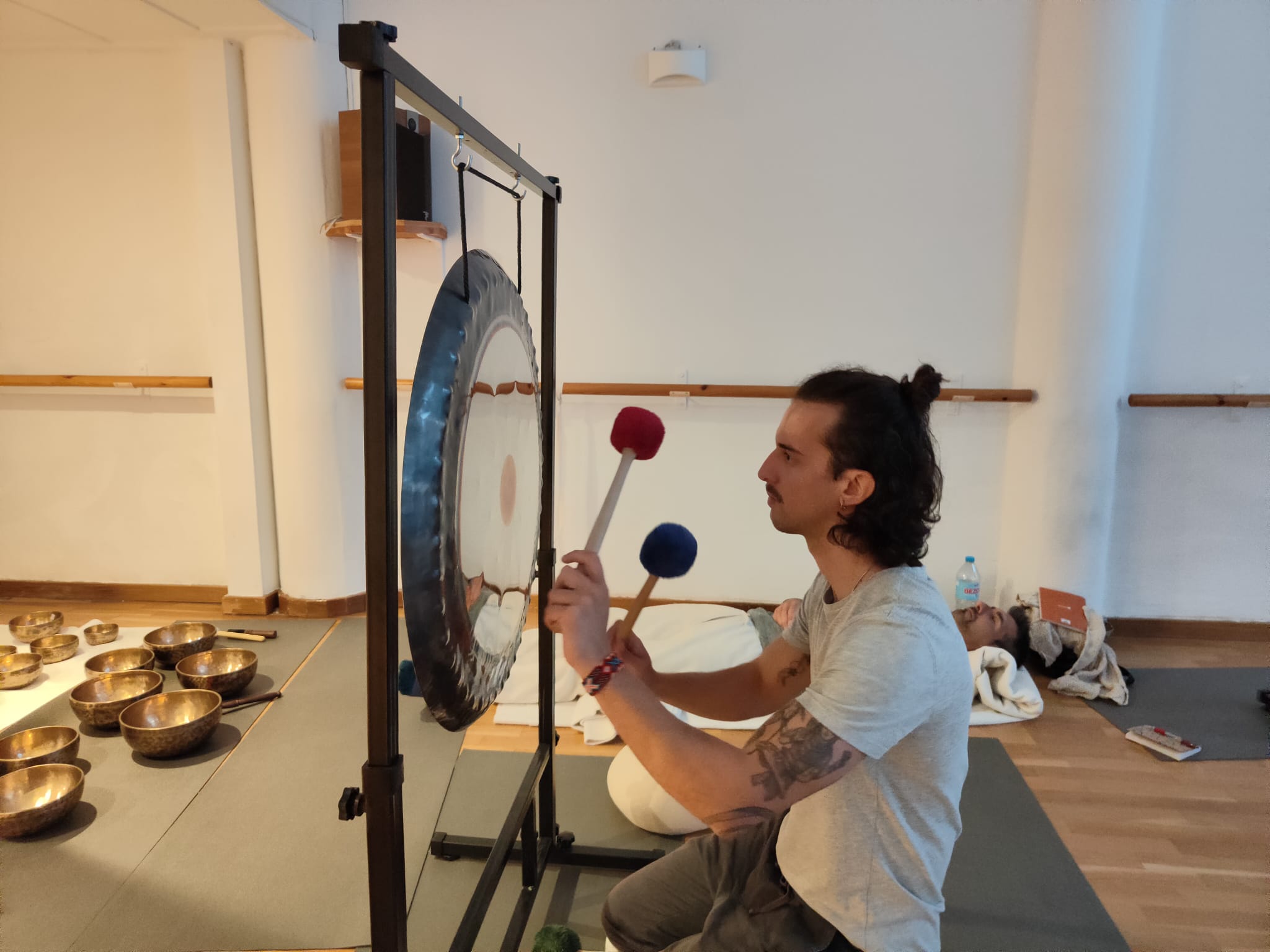 Ram Peris tocando el gong con dos mazas durante un baño de sonido con participante tumbado en Valencia