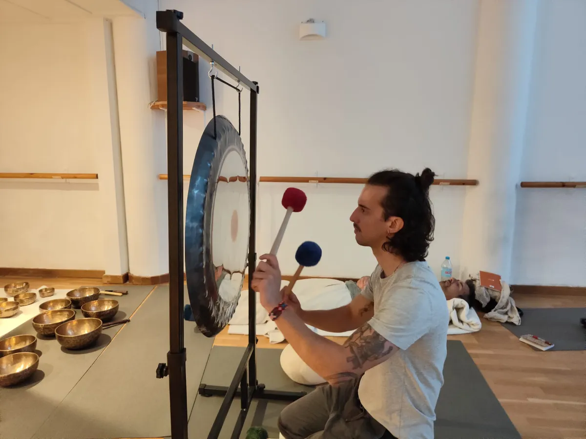 Ram Peris tocando el gong con dos mazas durante un baño de sonido con participante tumbado en Valencia